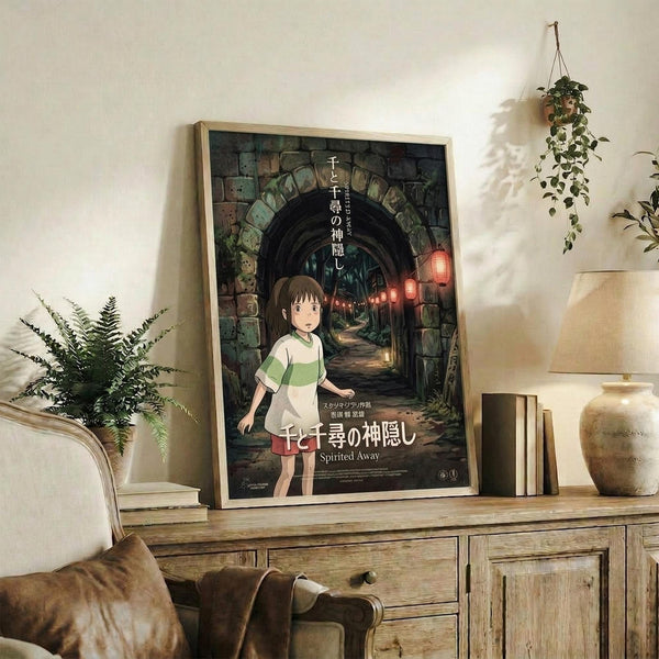May include: Framed Spirited Away movie poster featuring young girl character standing before stone archway tunnel with red lanterns, displayed on rustic wooden sideboard alongside potted ferns, books, ceramic vases, and hanging plant in cozy living room setting with beige chair visible.