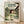 May include: Framed Studio Ghibli Spirited Away movie poster featuring Chihiro, a young girl with brown bob haircut wearing green and white striped shirt, standing in traditional Japanese garden setting with stone lanterns, pond, and wooden buildings. Poster displays Japanese and English text including "A Journey Beyond the Ordinary." Light wood frame rests against white wall on hardwood floor with natural lighting casting shadows.