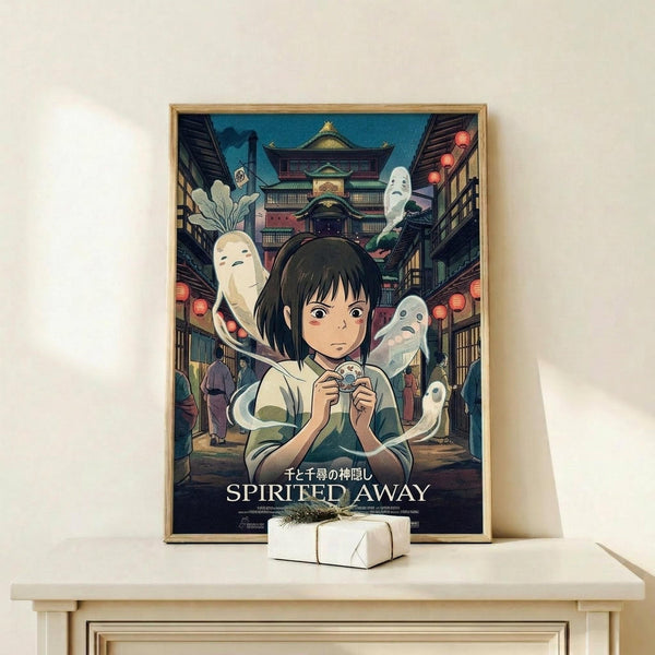 May include: Framed Spirited Away movie poster featuring young girl Chihiro surrounded by white spirits in traditional Japanese bathhouse setting with red lanterns and multi-story wooden architecture. Poster displayed on light wood shelf next to small white wrapped gift with twine and dried grass sprig against cream wall.