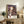 May include: Framed Spirited Away movie poster featuring Chihiro holding a white paper lantern against a backdrop of the elaborate bathhouse building with purple twilight sky. The poster sits on a rustic wooden sideboard alongside books, a ceramic vase, and fern plant in a cozy living room with cream armchair and warm lighting.