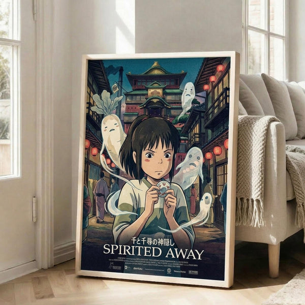 May include: Framed Studio Ghibli Spirited Away movie poster leaning against white wall in bright living room. Shows young girl with dark hair surrounded by ghostly spirits and traditional Japanese bathhouse architecture. Colorful anime artwork in light wood frame placed on hardwood floor next to beige couch with throw blanket. Natural sunlight streaming through windows creates warm, cozy home decor setting.