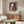 May include: Framed Spirited Away movie poster featuring Chihiro holding a paper lantern against a backdrop of the magical bathhouse, displayed above a mid-century modern walnut credenza in a minimalist living room with cream walls, white upholstered chair, and glass coffee table with colorful abstract art reflection.