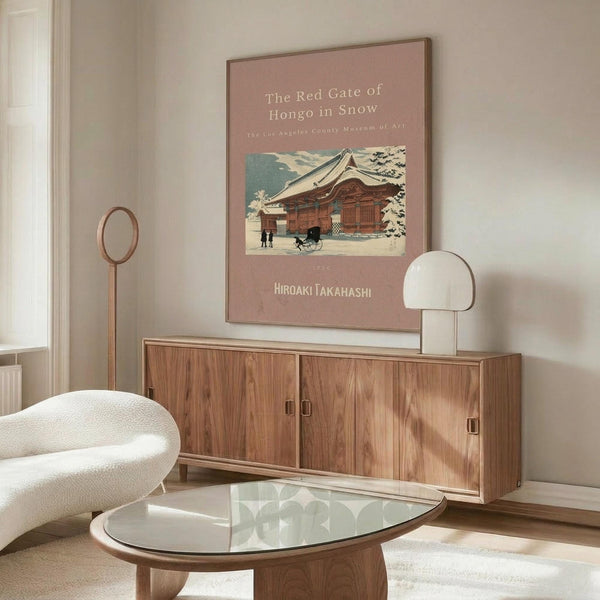 May include: Vintage Japanese woodblock print poster displayed above wooden sideboard in minimalist living room. Artwork shows traditional temple building with red gate in snowy winter scene, set against dusty rose background with white text. Modern furniture includes cream curved chair, glass oval coffee table, and wooden floor lamp. Natural lighting creates warm, contemporary atmosphere.