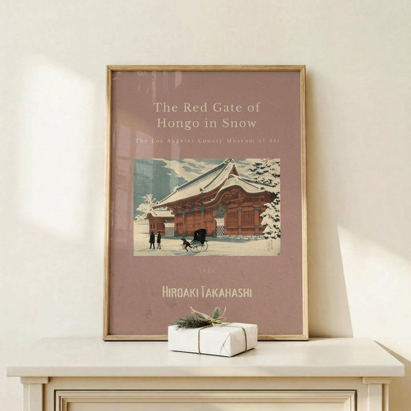May include: Framed vintage Japanese woodblock print poster displayed on light wood console table against cream wall. Art shows traditional red temple building in snow with small figures and rickshaw, set on mauve background with white text. Natural wood frame, small wrapped gift with greenery sits beside poster.