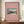 May include: Framed poster with pink background featuring vintage Japanese woodblock print of snow-capped Mt. Fuji, lake, and trees. White text shows artwork title and artist name Hiroaki Takahashi. Brown wooden frame sits on wooden credenza beside white ceramic vase and stacked books against cream walls with white molding.