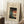 May include: Framed Japanese woodblock print showing blue morning glory flowers and white bellflowers beside a red paper lantern with black silhouettes, displayed on white shag rug against light walls. Wooden frame with cream matting, coffee cup on wooden stool nearby, cozy bedroom corner setting with natural lighting creating soft shadows.