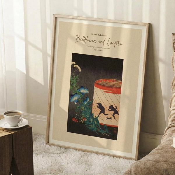 May include: Framed Japanese woodblock print showing blue morning glory flowers and white bellflowers beside a red paper lantern with black silhouettes, displayed on white shag rug against light walls. Wooden frame with cream matting, coffee cup on wooden stool nearby, cozy bedroom corner setting with natural lighting creating soft shadows.