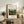 May include: Framed art print featuring Henri Rousseau's lush tropical jungle scene with dense green foliage, red flowers, and monkeys, displayed on a rustic wooden credenza alongside books, a fern plant, and ceramic vase in a warm, naturally-lit living room with neutral walls and upholstered furniture.