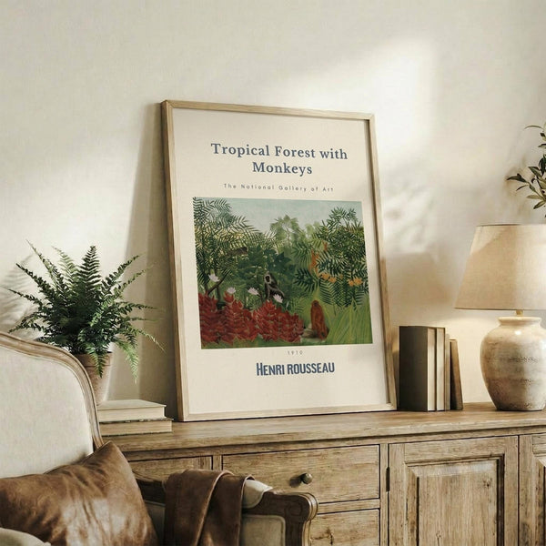 May include: Framed art print featuring Henri Rousseau's lush tropical jungle scene with dense green foliage, red flowers, and monkeys, displayed on a rustic wooden credenza alongside books, a fern plant, and ceramic vase in a warm, naturally-lit living room with neutral walls and upholstered furniture.