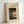 May include: Framed museum poster featuring Japanese woodblock print style artwork with blue bellflowers and green foliage on left side, red paper lantern with black silhouettes on right side, displayed in light wooden frame against white wall in bright interior setting