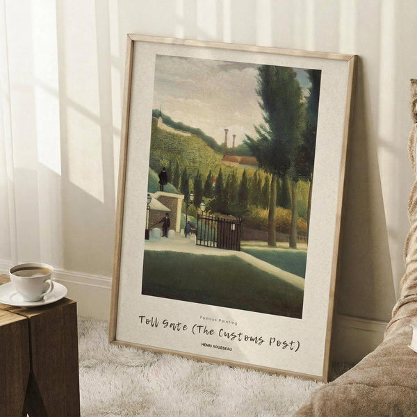 May include: Framed art print leaning against white wall corner on textured cream rug, showing Henri Rousseau's naive-style painting of a toll gate with lush green foliage, rolling hills, and small figures. Light wood frame with white matting displays the artwork beside a coffee cup on wooden block. Natural lighting creates soft shadows on wall.
