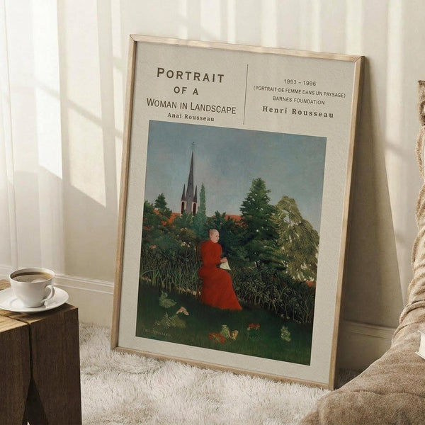 May include: Framed art print leaning against white wall corner showing woman in red dress sitting in lush green landscape with church spire in background. Light wood frame on white mat, positioned on textured cream rug next to wooden stool with white coffee cup and saucer.