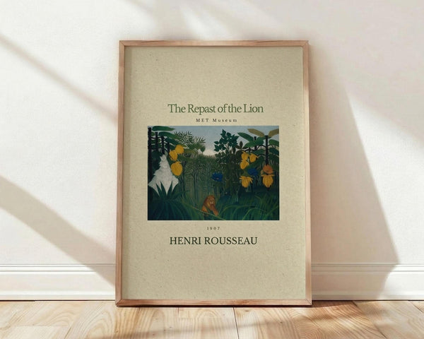 May include: Framed art print featuring Henri Rousseau's jungle scene with lush green foliage, yellow flowers, and a reclining lion among tropical plants. The poster has cream-colored background with dark text reading "The Repast of the Lion," "MET Museum," "1907," and "HENRI ROUSSEAU." Wood frame leans against white wall on light wooden floor with soft natural lighting creating diagonal shadows.