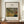 May include: Framed art print displaying Henri Rousseau's tropical jungle painting featuring a tiger among lush green foliage, mounted in thin wooden frame on wooden credenza beside white ceramic vase and books against cream paneled wall