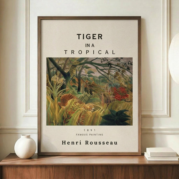 May include: Framed art print displaying Henri Rousseau's tropical jungle painting featuring a tiger among lush green foliage, mounted in thin wooden frame on wooden credenza beside white ceramic vase and books against cream paneled wall