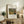 May include: Framed art print featuring Henri Rousseau's tropical jungle painting with tiger, displayed on rustic wooden sideboard alongside fern plant, ceramic vase, and stacked books in warm, naturally-lit living room setting with cream armchair and neutral walls
