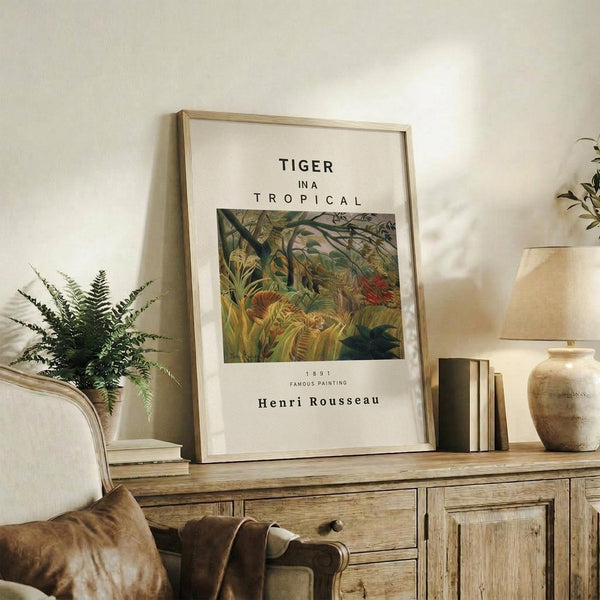 May include: Framed art print featuring Henri Rousseau's tropical jungle painting with tiger, displayed on rustic wooden sideboard alongside fern plant, ceramic vase, and stacked books in warm, naturally-lit living room setting with cream armchair and neutral walls