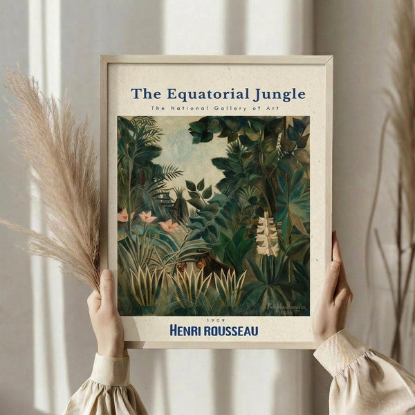 May include: Hands holding a framed art print featuring Henri Rousseau's lush jungle painting with dense green tropical foliage, palm fronds, and pink flowers. The cream-colored poster has museum-style text at top and bottom. Person wears a beige ruffled sleeve shirt and holds dried pampas grass stems. Soft natural lighting against white curtains creates an elegant, minimalist styling setup.