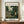 May include: Framed vintage art poster featuring a lush tropical jungle scene with dense green foliage, palm fronds, flowering plants in pink and white, displayed on a wooden console table beside a cream ceramic vase and stacked books against white paneled walls in a bright, minimalist room setting.