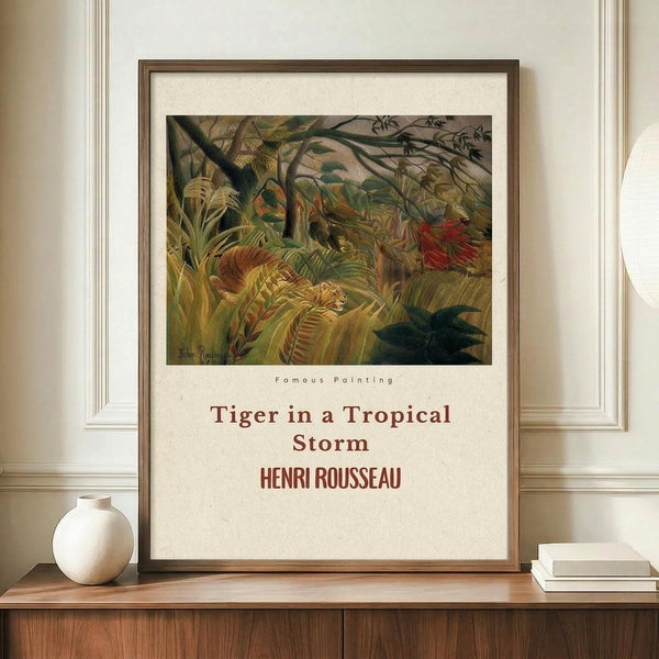 May include: Framed art print featuring Henri Rousseau's jungle painting with a tiger hidden among lush green tropical foliage and palm fronds during a storm. The poster has cream-colored text below the artwork identifying the title and artist. Displayed on a wooden sideboard beside a white ceramic vase and stacked books in an elegant room with cream walls and white molding.