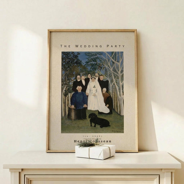 May include: Framed art print featuring Henri Rousseau's primitive style painting of a wedding party in a forest setting. The artwork shows figures in formal black attire surrounding a bride in white, with a black dog at their feet and leafy trees in the background. The print has cream matting with black text above and below the image. A small wrapped gift with twine and greenery sits on a light wood console table beneath the frame against a white wall.