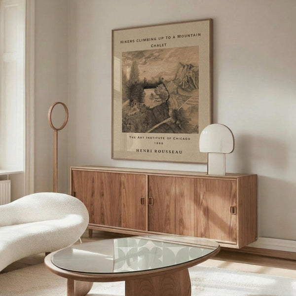 May include: Henri Rousseau vintage art print featuring hikers climbing toward a mountain chalet, displayed in thin wooden frame above walnut sideboard in modern neutral living room with white sculptural chair, glass oval coffee table, and warm natural lighting