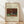 May include: Framed art print leaning against white wall on light wood floor. The poster shows a realistic painting of a gray and white rabbit sitting beside orange carrots and green cabbage leaves, with a brick wall and tree branch in the background. Cream-colored mat with black text identifying the artwork as Henri Rousseau's 1908 piece. Natural wood frame with visible grain, soft window light creating diagonal shadows across the white fabric backdrop.