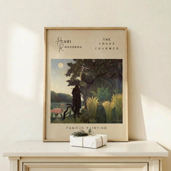 May include: Framed art print featuring Henri Rousseau's jungle scene with silhouetted figure among tropical foliage, flamingos by water, and full moon in dusky sky. Natural wood frame on light wooden surface with small wrapped gift box beside it. Cream colored wall background with soft natural lighting.