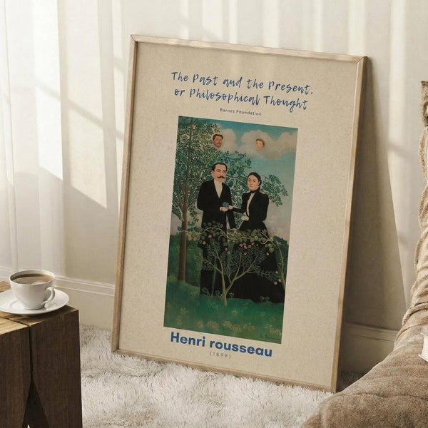 May include: Framed vintage art poster leaning against white paneled wall on white textured rug. Print shows two men in dark formal wear standing beneath green trees with two faces floating in blue sky above. Text reads "The Past and the Present, or Philosophical Thought" and "Henri Rousseau (1890)" in blue lettering on cream background. Natural wood frame, cozy room setting with coffee cup on wooden block nearby and beige blanket.