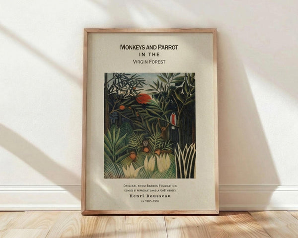 May include: Framed art print leaning against white wall on light wood floor. Print shows Henri Rousseau's jungle painting with dense green foliage, orange fruits, monkeys, and a red-orange parrot. Natural wood frame surrounds cream matting with black text above and below the artwork. Soft natural lighting creates diagonal shadows across the scene.