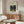May include: Framed Henri Rousseau jungle print featuring monkeys and parrot among lush green foliage, displayed above walnut credenza in modern living room with white curved chair, glass oval coffee table, and minimalist decor. Print shows tropical birds in dense forest setting with museum-style text layout.