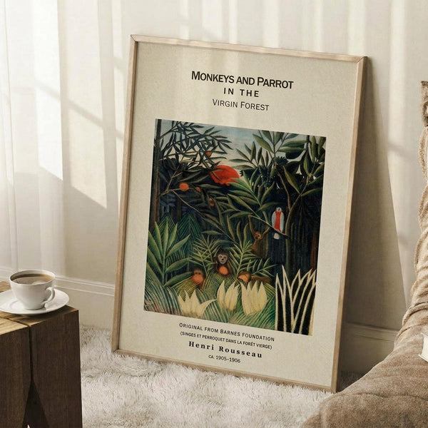 May include: Framed art print leaning against white wall showing tropical jungle scene with monkeys and red parrot among lush green foliage. Print has cream matting with black text identifying it as Henri Rousseau artwork from Barnes Foundation, dated ca. 1905-1906. Scene shows coffee cup on wooden surface and textured beige throw blanket nearby.