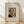 May include: Framed art print of Henri Rousseau's self-portrait showing a balding man with dark mustache wearing formal black suit with bow tie, positioned next to an oil lamp. The vintage-style poster has cream matting with elegant typography above and below the image. Natural wood frame leans against white wall on light wooden floor with soft shadows from window light.