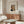 May include: Henri Rousseau self-portrait poster displayed in modern living room with warm wood sideboard, white sculptural chair, glass oval coffee table, and mushroom table lamp. The vintage art print shows a man with mustache in formal attire, framed in thin wood frame against neutral beige walls with natural lighting.