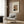 May include: Vintage art poster featuring Henri Rousseau's self-portrait displayed in modern living room with beige armchair, geometric patterned pillow, brass floor lamp, and dark wood wall paneling. The framed print shows a mustachioed man in dark clothing against cream matting with vintage typography above and signature below.