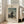 May include: Framed art print leaning against white wall next to beige sofa in bright living room with large windows. Print shows Henri Rousseau's 1890 self-portrait featuring man in black suit and beret holding palette, standing before landscape with buildings and cloudy sky. Cream matting with black text including "MYSELF PORTRAIT LANDSCAPE" and artist name.