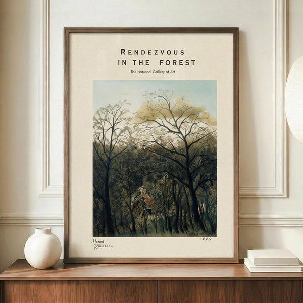 May include: Framed art print displayed on wooden sideboard featuring dense forest scene with bare branching trees, lush green foliage, and small figures visible in clearing. Cream matting surrounds artwork in thin brown frame. White ceramic vase and stacked books sit alongside on warm wood surface against cream paneled wall.