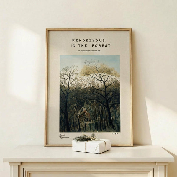 May include: A framed art print displaying a lush forest scene with bare branched trees in the foreground and dense green foliage beyond, set in a light wood frame on a cream-colored surface. A small white gift box with twine and evergreen sprig sits beside the frame against a neutral wall with soft natural lighting.