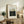 May include: Framed art print featuring a lush forest scene with tall trees and foliage in green and blue tones, displayed on a rustic wooden sideboard alongside books, a fern plant, ceramic vase, and table lamp in a cozy living room setting with neutral walls and upholstered furniture.
