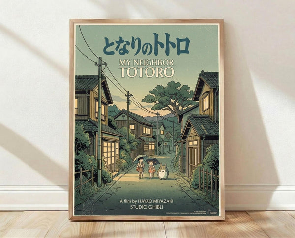 May include: Framed poster print in light wood frame leaning against white wall on wooden floor. Artwork shows Studio Ghibli's My Neighbor Totoro in vintage travel poster style with muted green and yellow tones. Scene depicts traditional Japanese village street at dusk with two children and Totoro character standing under power lines between wooden houses with glowing windows and lush trees.
