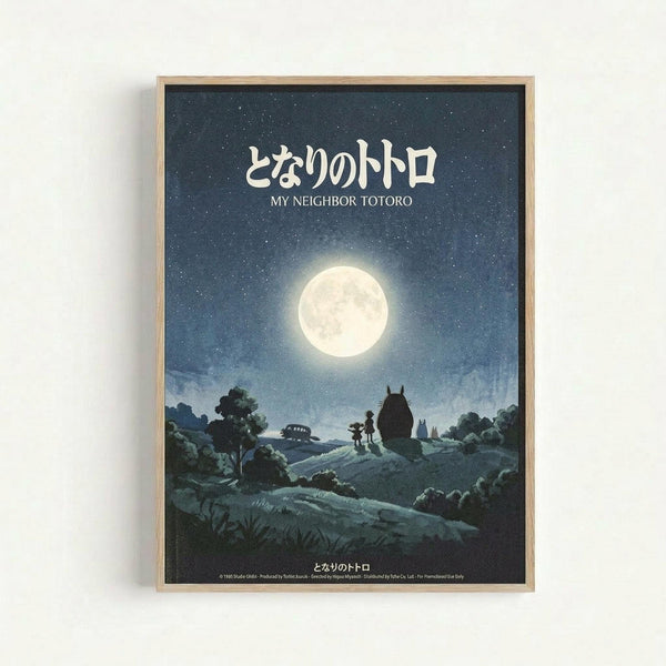 A framed poster featuring a moonlit night scene with two small children standing beside the large, round silhouette of Totoro on a hillside. The full moon illuminates a starry blue sky above rolling countryside with trees, and a small bus is visible in the distance. Japanese text and "MY NEIGHBOR TOTORO" appear at the top in white lettering. The artwork has a dreamy, nostalgic animation style in blue and cream tones, displayed in a light wood frame against a white wall.
