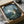 May include: Framed My Neighbor Totoro poster being unboxed from brown cardboard shipping package with white tissue paper. The vintage-style print shows the iconic gray forest spirit character standing in a moonlit landscape with glowing fireflies, rendered in muted blue and green tones. Black frame sits in open cardboard box on white surface next to partial view of dark bowl.