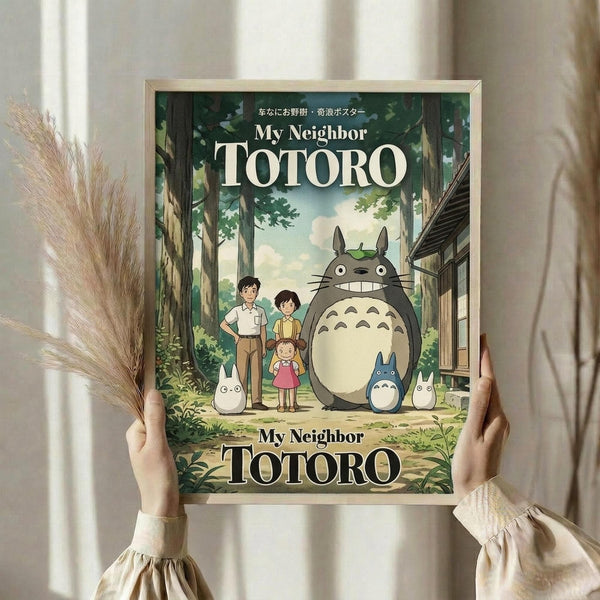 May include: Hands holding a framed poster featuring the beloved forest spirit Totoro with children in a lush green woodland setting. The vintage-style print shows the large grey creature alongside smaller white spirits and three children near a traditional wooden structure. Displayed against white curtains with dried pampas grass visible, creating a cozy home decor scene.