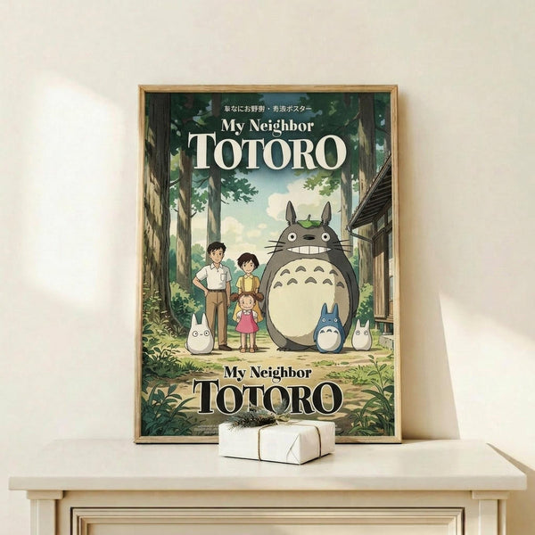 May include: Framed poster displaying animated forest scene with large gray creature, family of three people, and small white creatures among green trees. Wooden frame sits on light wooden shelf next to small white wrapped package against cream wall.