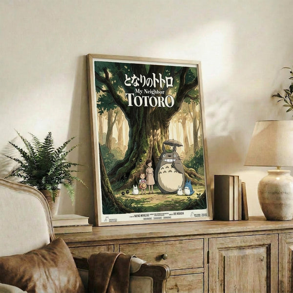 May include: Framed Studio Ghibli movie poster featuring Totoro and children under a large forest tree, displayed on rustic wooden sideboard with fern plant, books, ceramic vase, and beige armchair visible in cozy living room setting with neutral walls