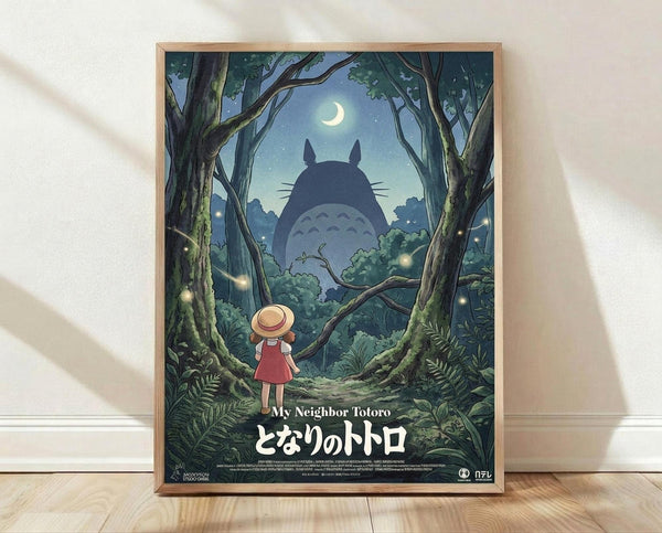 May include: Framed movie poster showing a young girl in red dress and straw hat standing in an enchanted moonlit forest, looking up at the large silhouette of Totoro among glowing fireflies and twisted tree branches. The artwork features deep blues and greens with Japanese text at bottom. The wooden-framed print leans against a white textured wall on light wooden flooring with soft natural lighting creating gentle shadows.