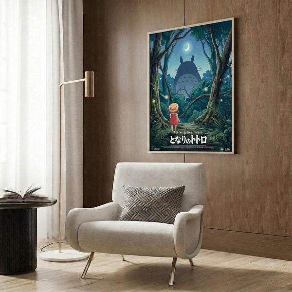 May include: Framed Studio Ghibli My Neighbor Totoro movie poster mounted on wood-paneled wall above cream upholstered armchair with geometric patterned pillow. Poster shows small girl in red dress looking up at large Totoro silhouette in moonlit forest scene with Japanese text below. Modern reading corner with brass floor lamp and open book on dark side table.
