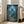 May include: Framed Studio Ghibli My Neighbor Totoro movie poster leaning against white wall next to beige sofa. Artwork shows small girl in red dress and hat looking up at large grey Totoro creature in moonlit forest with glowing fireflies among green trees. Japanese text at bottom. Natural lighting from nearby windows.