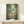 May include: Framed poster featuring characters from animated film in bamboo forest setting, displayed on light wood console table beside small white wrapped gift box against cream wall with natural lighting