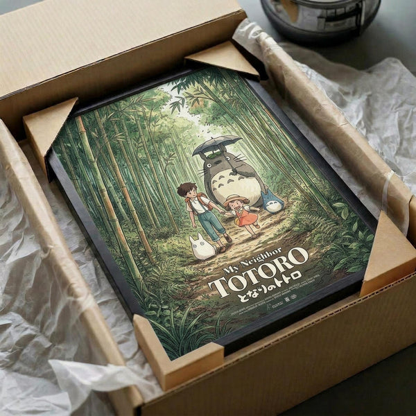 May include: Framed Studio Ghibli poster showing Totoro with umbrella standing beside two children on a forest path surrounded by tall green bamboo trees. The vintage-style print features muted earth tones and is displayed in a black frame, carefully packed in brown cardboard shipping box with protective tissue paper wrapping.